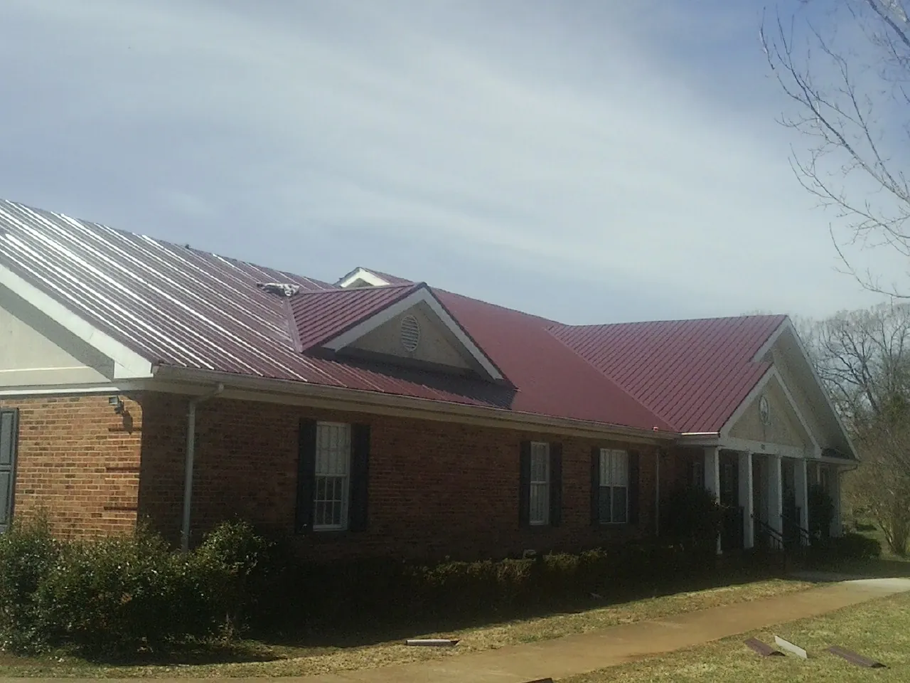 Red metal roof with gabled entries on a long brick building, from a Hail Damage Roof Repair job in Shinnston