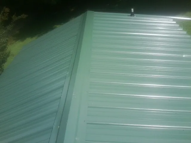 New green metal panels meeting at the ridge of a roof — Flat Roof Repair work by our crew in Shinnston
