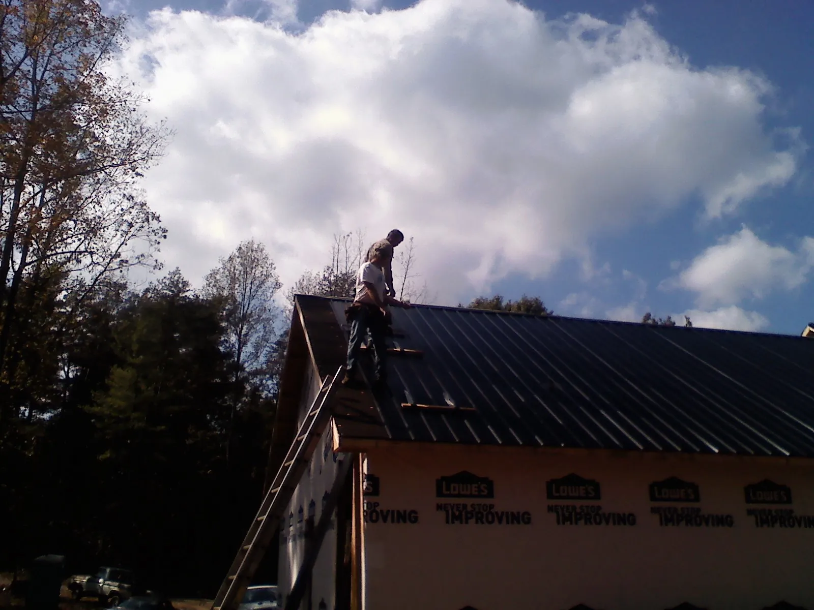 Roofer fastening dark metal panels high against a cloudy sky, from a Roof Inspection job in Shinnston