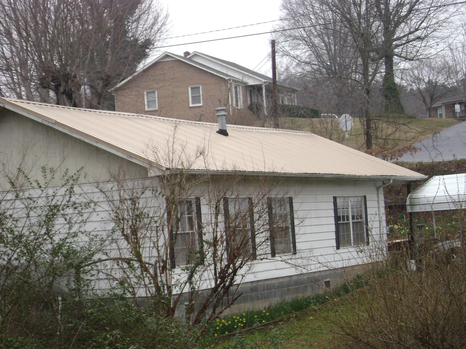 Tan metal roof on a white sided house set into a hillside — Commercial Roofing by Roofing Brothers in Shinnston
